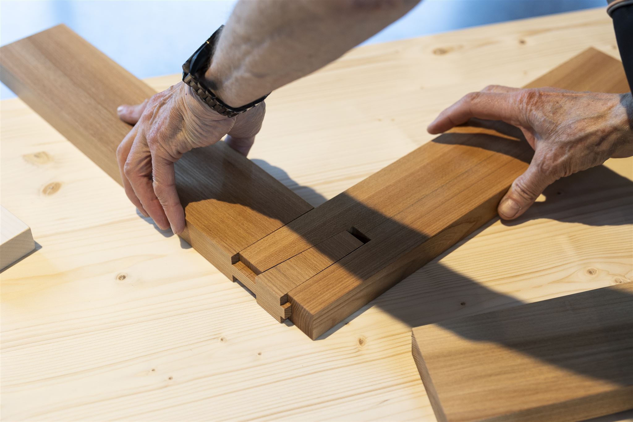 Hände die zwei Holzleisten mittels Holzverbindung zusammenstecken