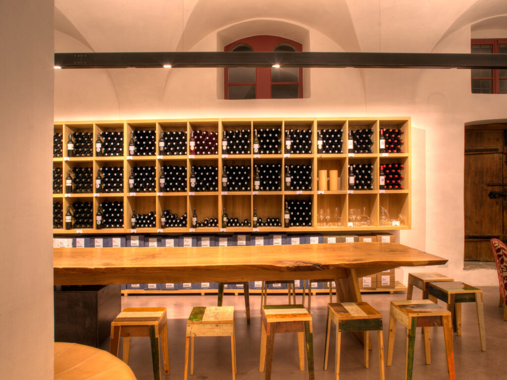 massiver Verkostungstisch aus einem Brett mit Baumkante mit Weinregal im Hintergrund.