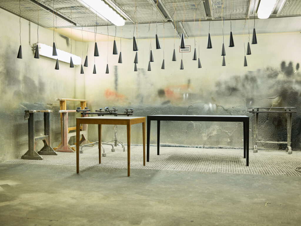 kleiner Tisch in Esche braun gebeizt und grosser Tisch in Esche schwarz lackiert mit heller Tischplatte vor bunt bespritzter Wand.