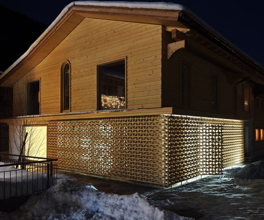 Holzhaus mit beleuchtetem, gitterförmigem Windfang bei Nacht und Schnee