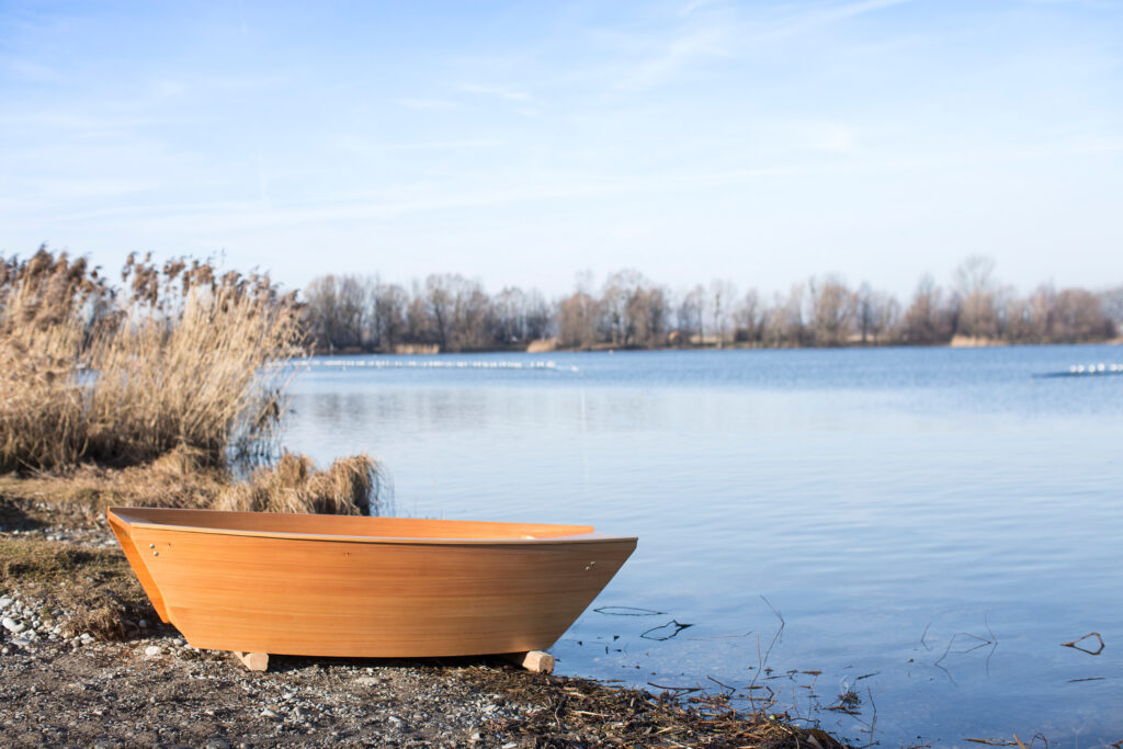 Holzbadewanne steht am Ufer eines Sees vor Schilf.